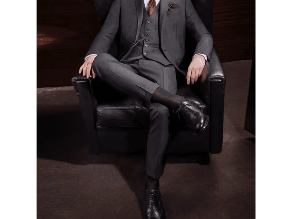 Người đàn ông mặc suit, ngồi bắt chéo chân, để lộ phần tất cổ cao tối màu, liền mạch và hài hòa với quần